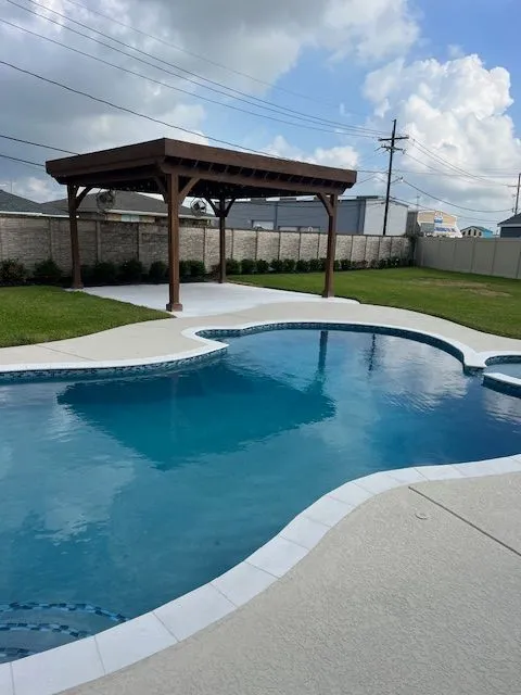 Swimming pool with a wooden pergola, surrounded by grass and a concrete patio.
